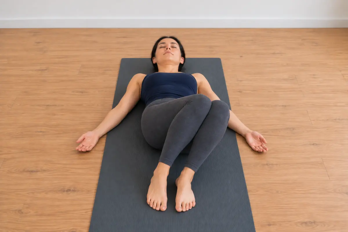 A woman lying on her back on a yoga mat, seen from above her feet, with her feet flat and her knees together tipped a short way to one side, shoulders flat.